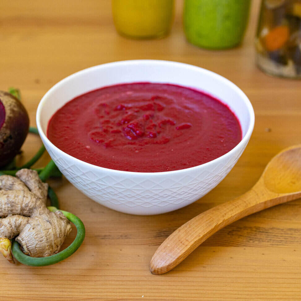 Geometric bowl, wooden spoon, herbs; vibrant beet-coconut-ginger soup.