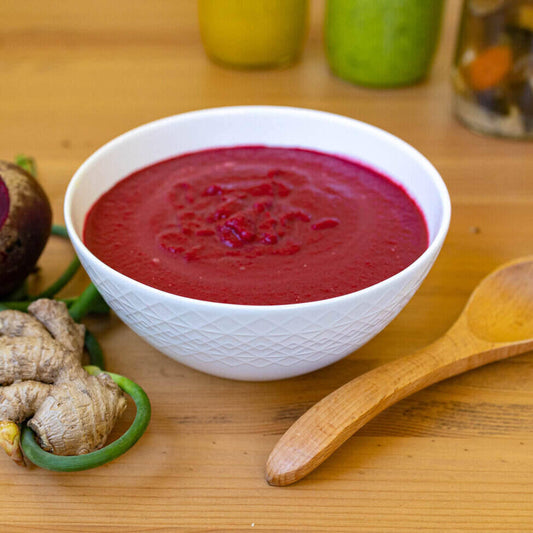 Geometric bowl, wooden spoon, herbs; vibrant beet-coconut-ginger soup.