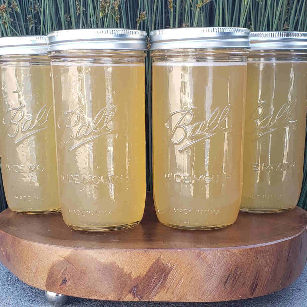 Four Ball mason jars of a clear brown soup - bone broth- sit on a wooden board.