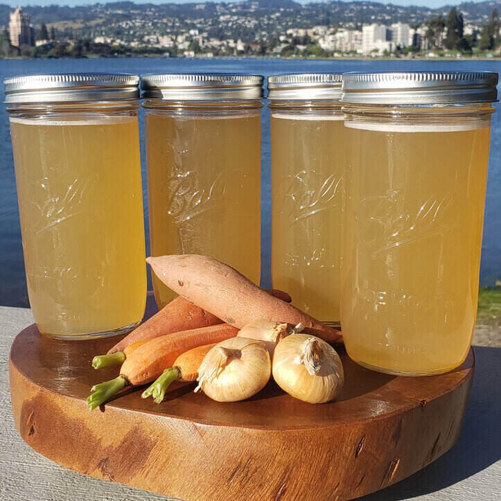 Four Ball mason jars of a clear brown soup - bone broth- sit on a wooden board.
